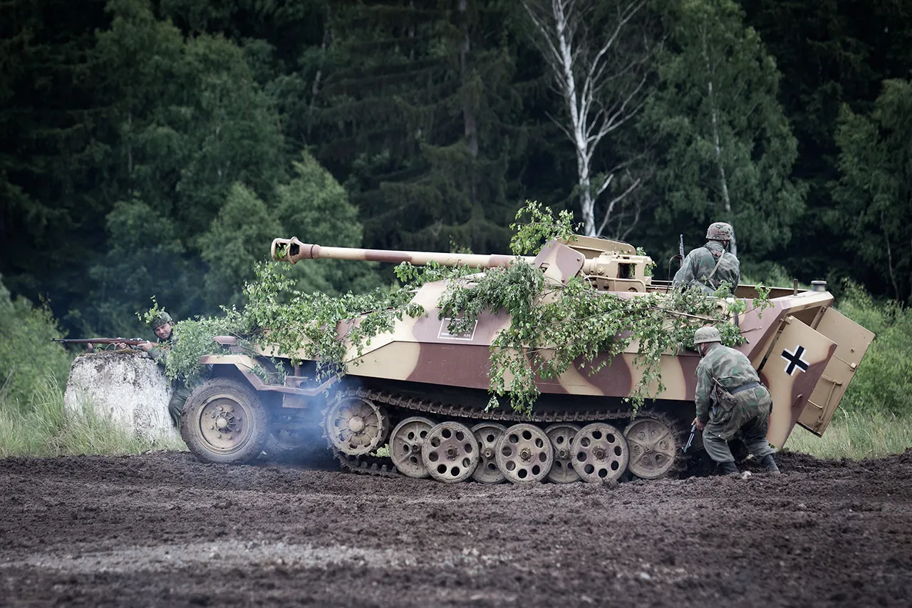 Kryjící se voják v německé uniformě doprovází obrněný transportér Sd.Kfz. 251 v blátivém prostředí, v pozadí les, rekonstukce bitvy z 2. světové války, akce Bahna